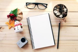 workspace-desk-with-notebook-pencil-pine-cones-in-tea-wooden-cup-eye-glasses-christmas-decoration-and-small-action-camera-on-wooden-background